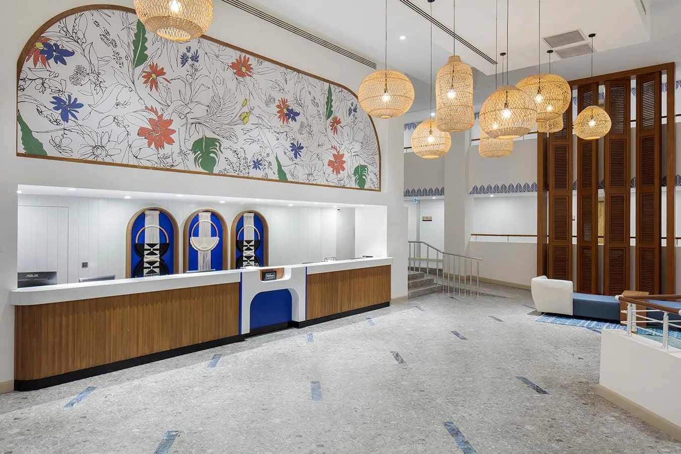 Reception desk in the lobby of DoubleTree by Hilton Torba Işıl Club, with a floral mural above it and rattan pendant lights